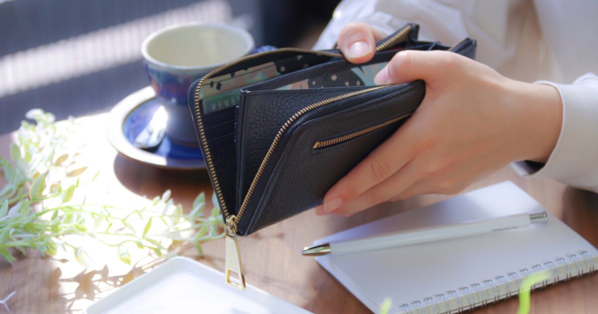 開いた財布とノートが置かれたテーブルで家計管理する様子